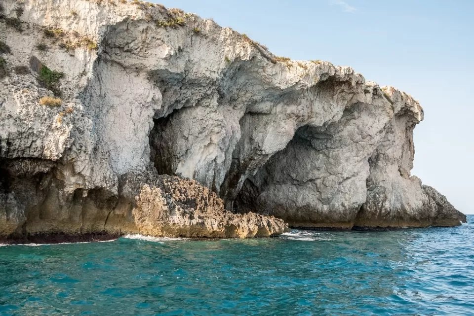 Una grotta marina scavata in una scogliera chiara, con il mare turchese davanti